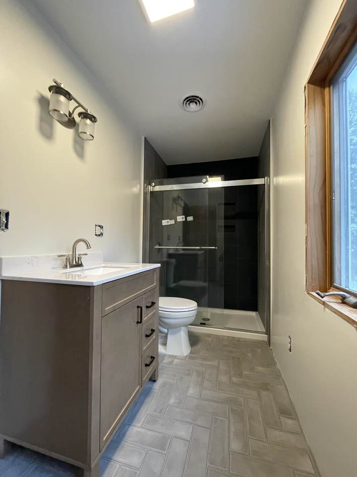Remodeled bathroom with new vanity, herringbone tile floor, and glass shower