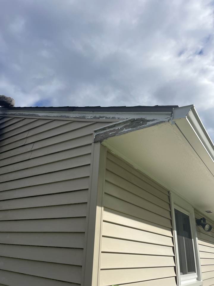 Peeling and rotted fascia board at a roof corner before repair