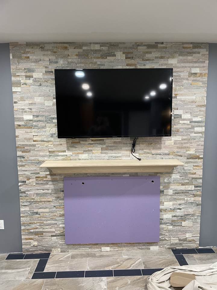 Stone veneer fireplace wall with mounted TV and wood mantel