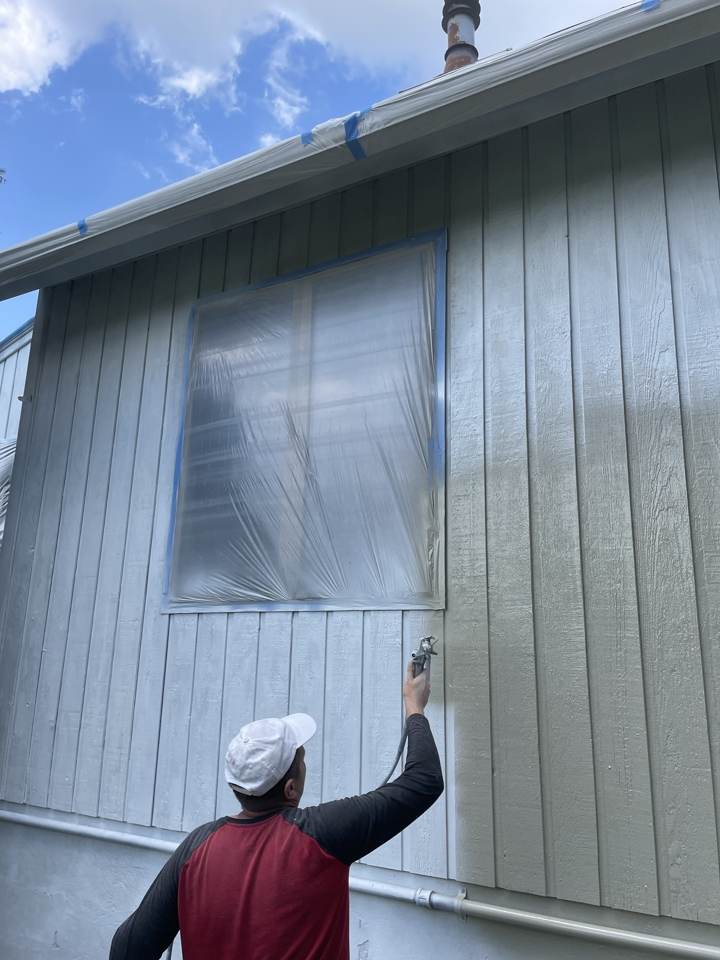 Painter spray painting wood siding on a house exterior